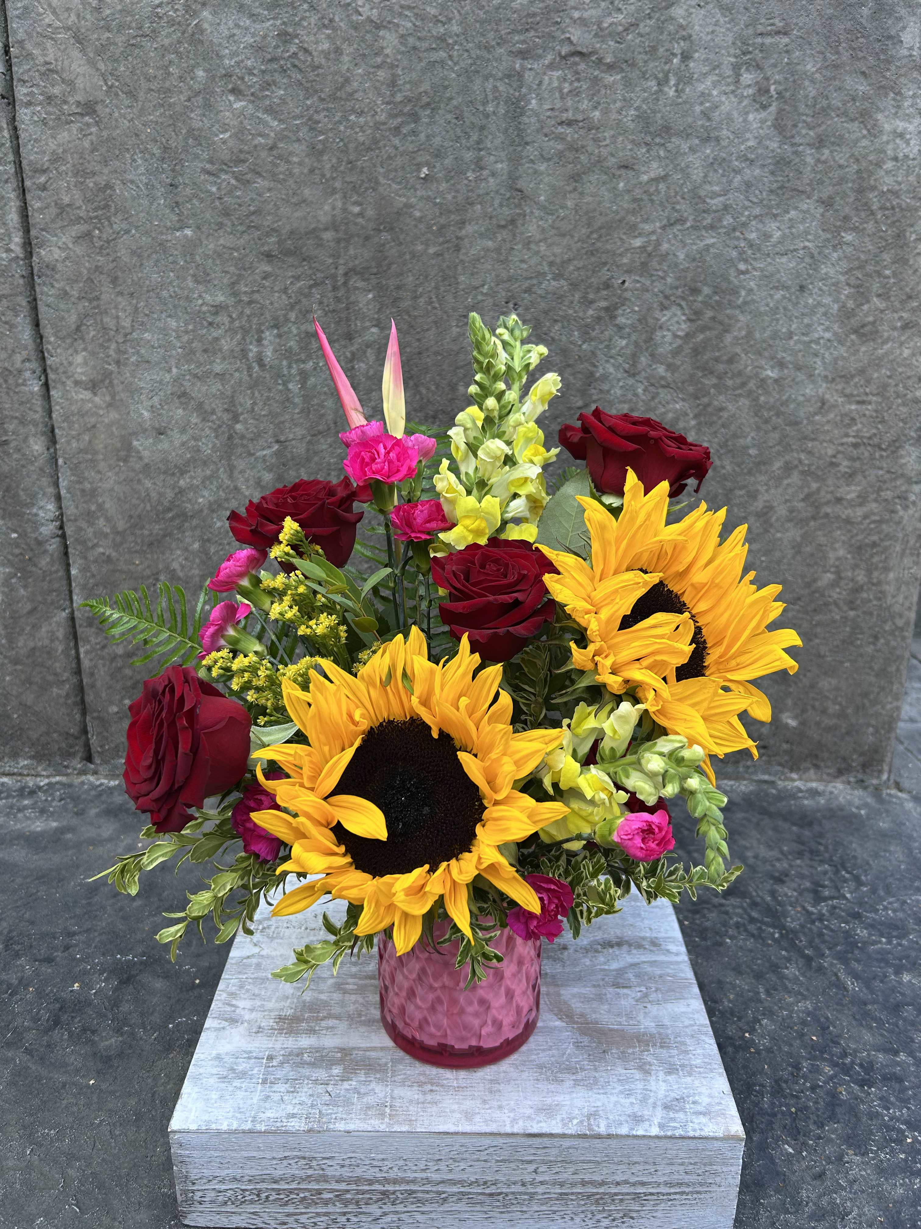 Bouquet of sunflowers, red roses, and pink flowers in a pink vase