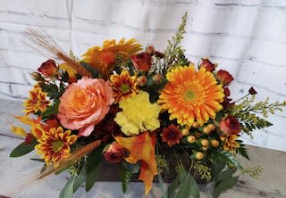 Autumn floral arrangement with orange and yellow blooms in a low container