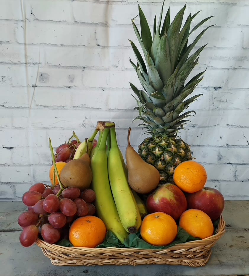 Basket of assorted fruit with a pineapple, bananas, grapes, pears, oranges, and apples