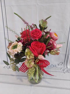 Bouquet of red roses and mixed pink flowers in a glass vase with a red ribbon