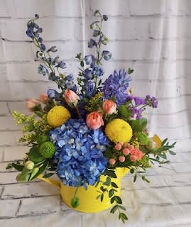 Colorful flower arrangement in a yellow container with blue hydrangea and mixed blooms