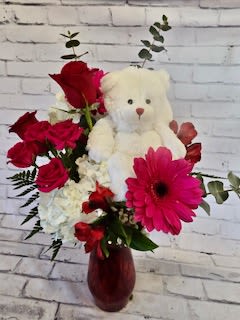 Red flowers arranged with a white teddy bear in a vase