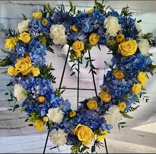 Heart-shaped floral wreath with blue, yellow, and white flowers on an easel