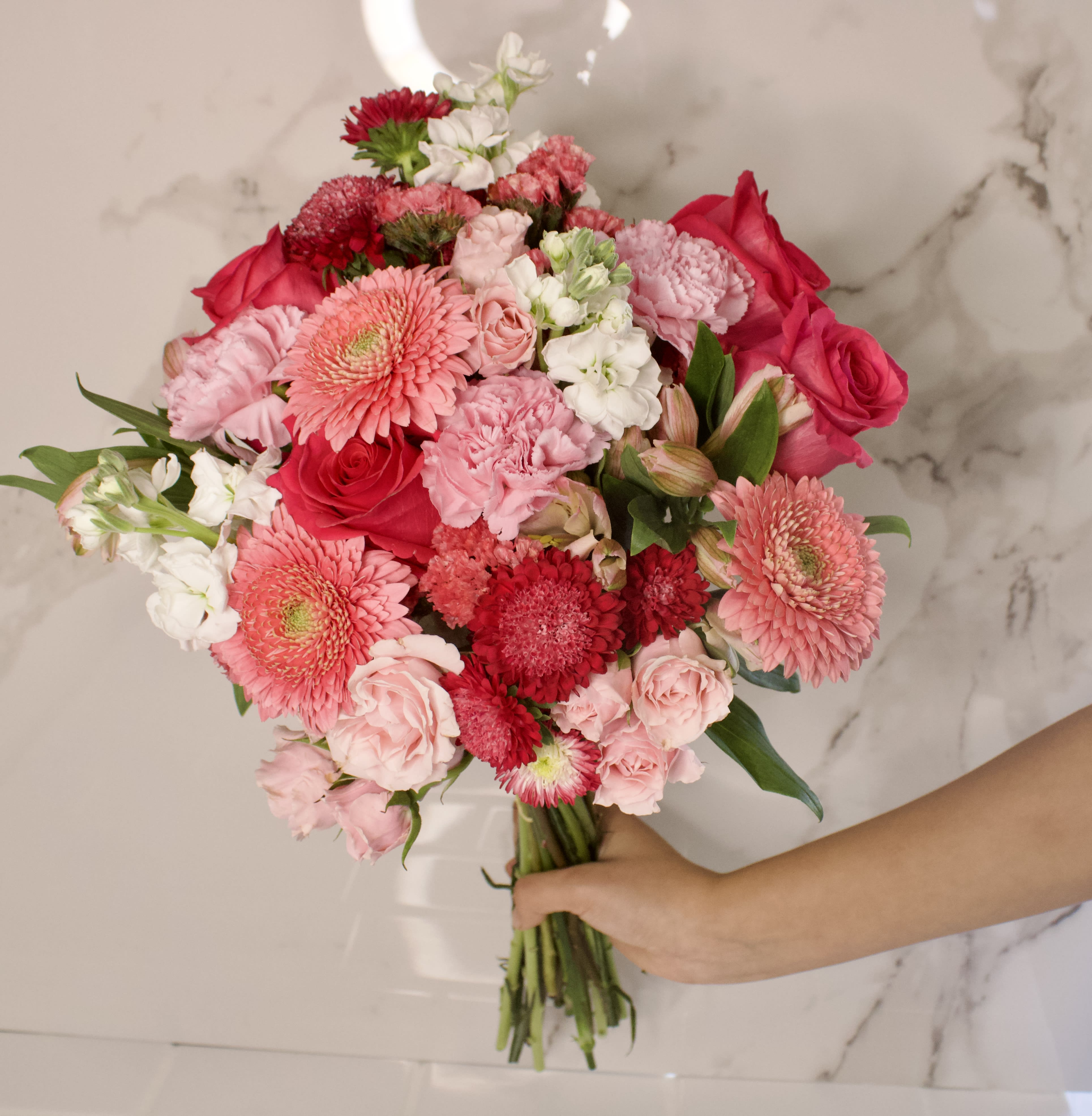 Handheld bouquet of pink and red flowers with white accents