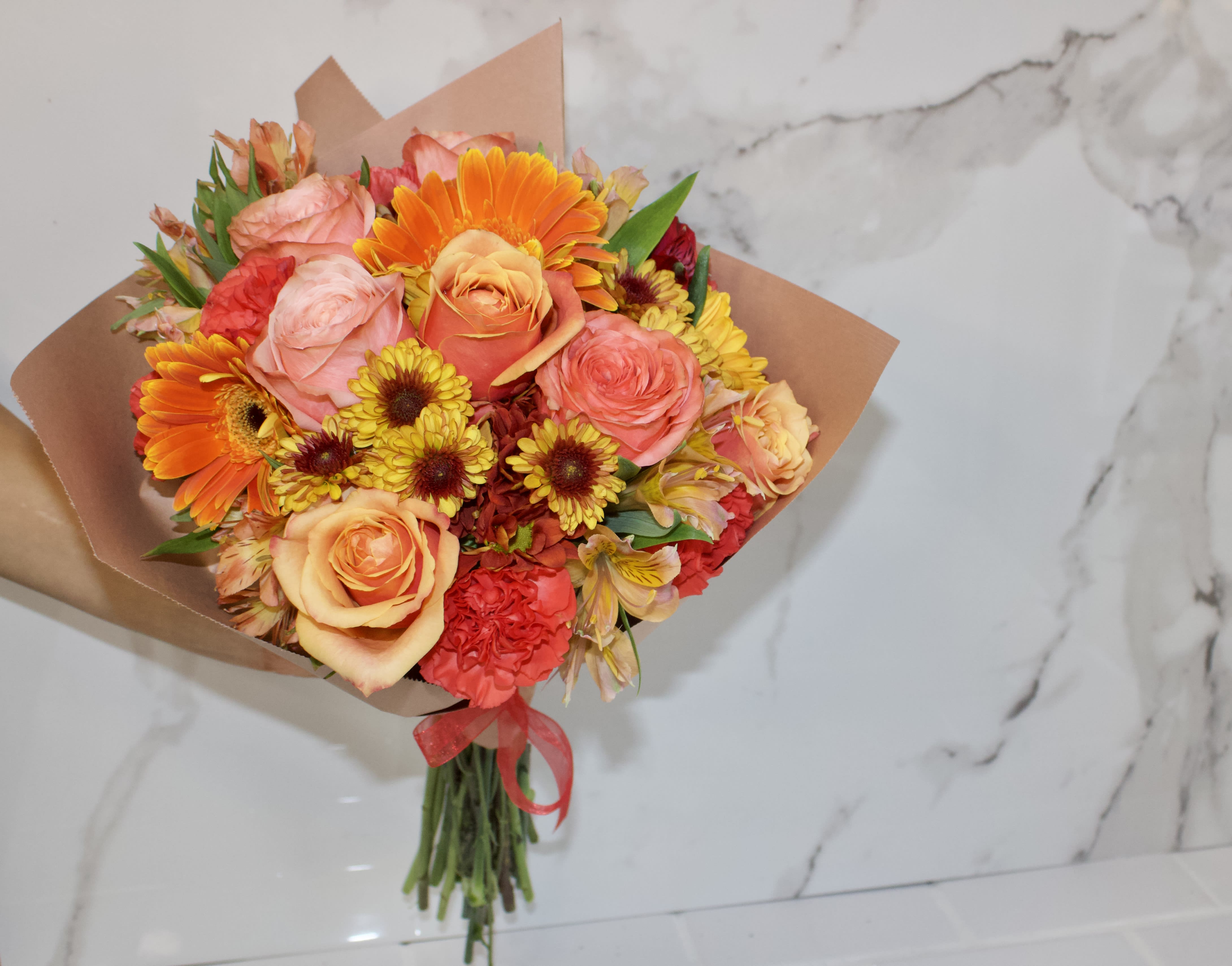 Bouquet of orange, pink, and yellow flowers wrapped in brown paper