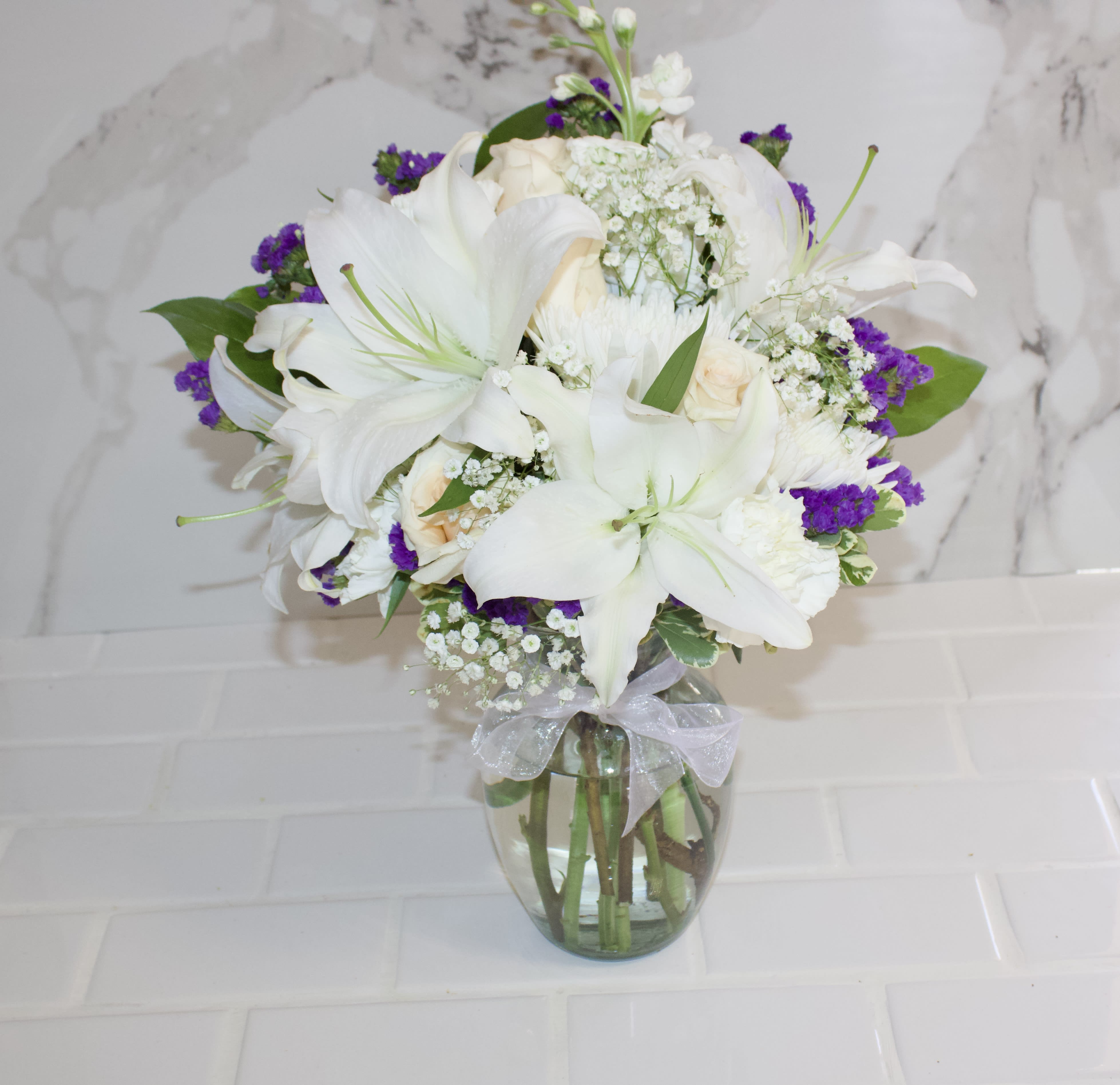 White lilies and roses in a glass vase with purple filler flowers