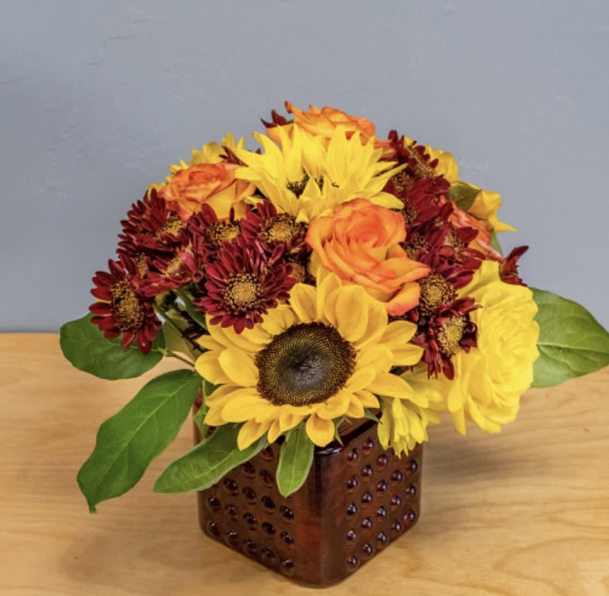 Sunflowers, roses, and mums arranged in a square brown vase
