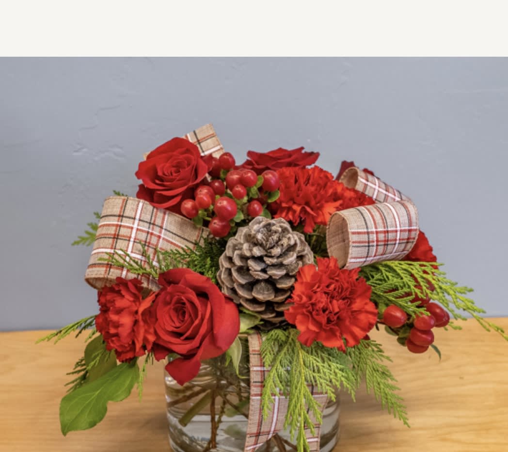 Red roses and carnations arranged in a glass vase with plaid ribbon and a pinecone