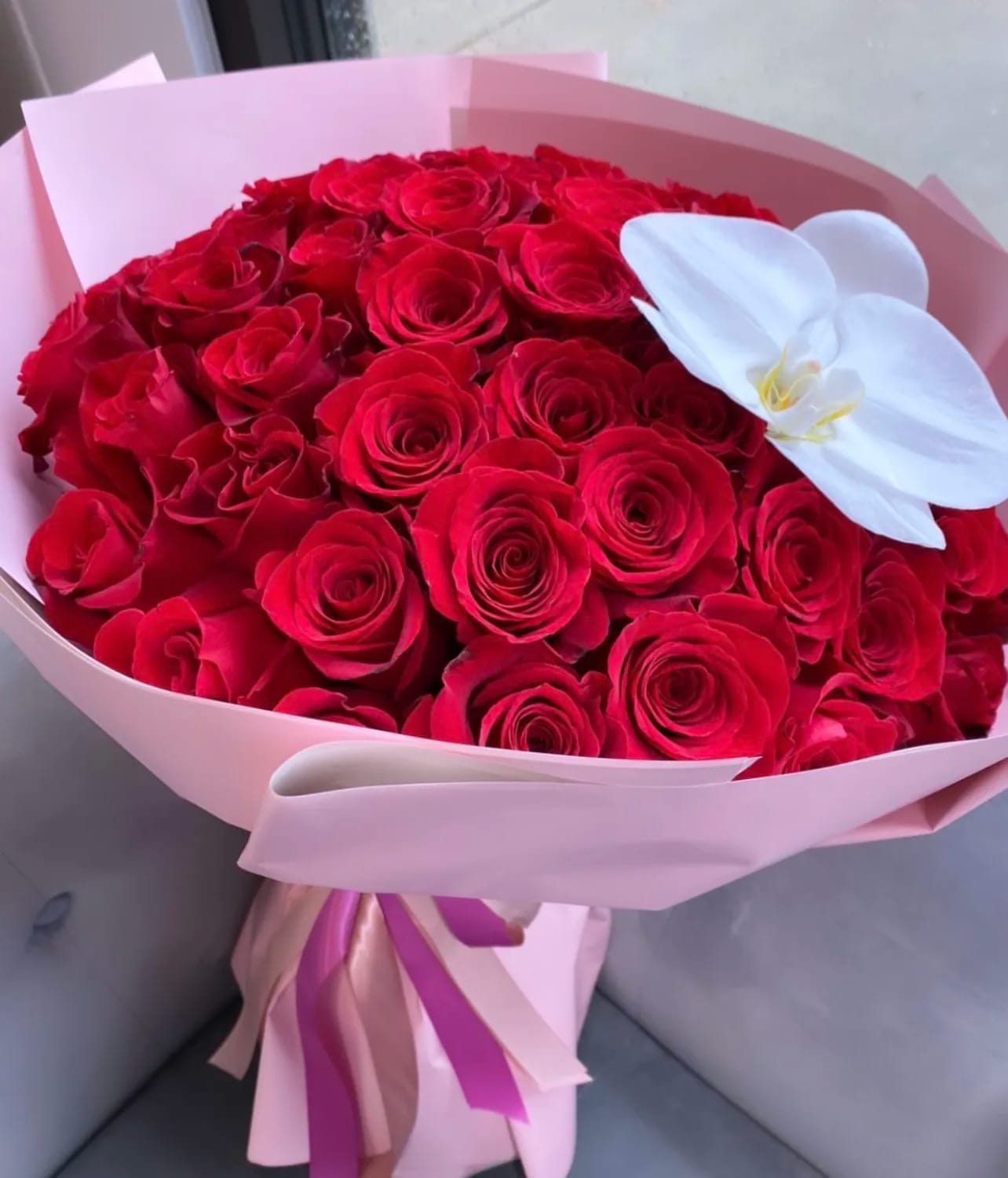 Bouquet of red roses with a white orchid accent in pink wrapping