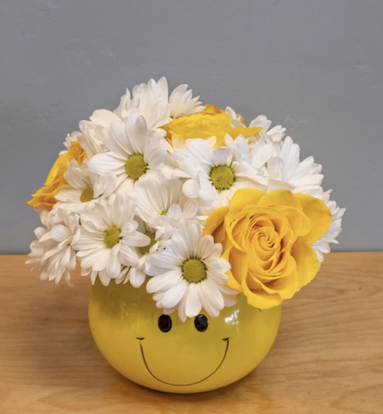 Yellow smiley-face vase holding white daisies and yellow roses