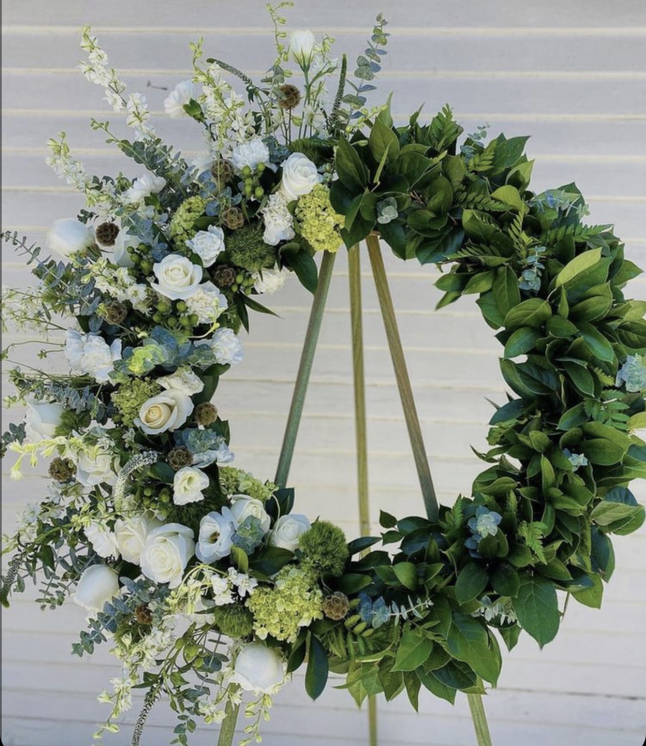 Floral wreath with white roses and greenery on a stand