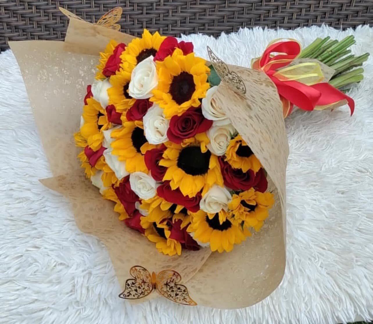 Bouquet of sunflowers and red and white roses wrapped in tan paper