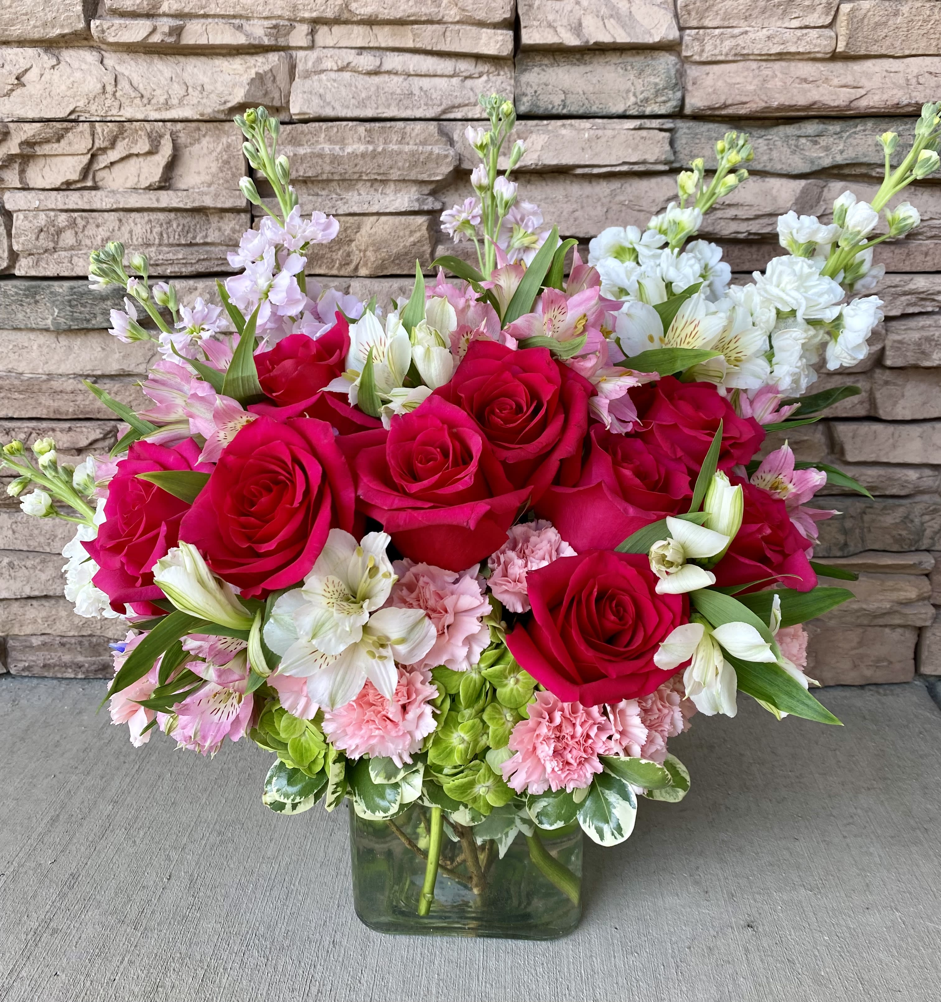 Bouquet of red roses, pink carnations, and white alstroemeria in a glass vase