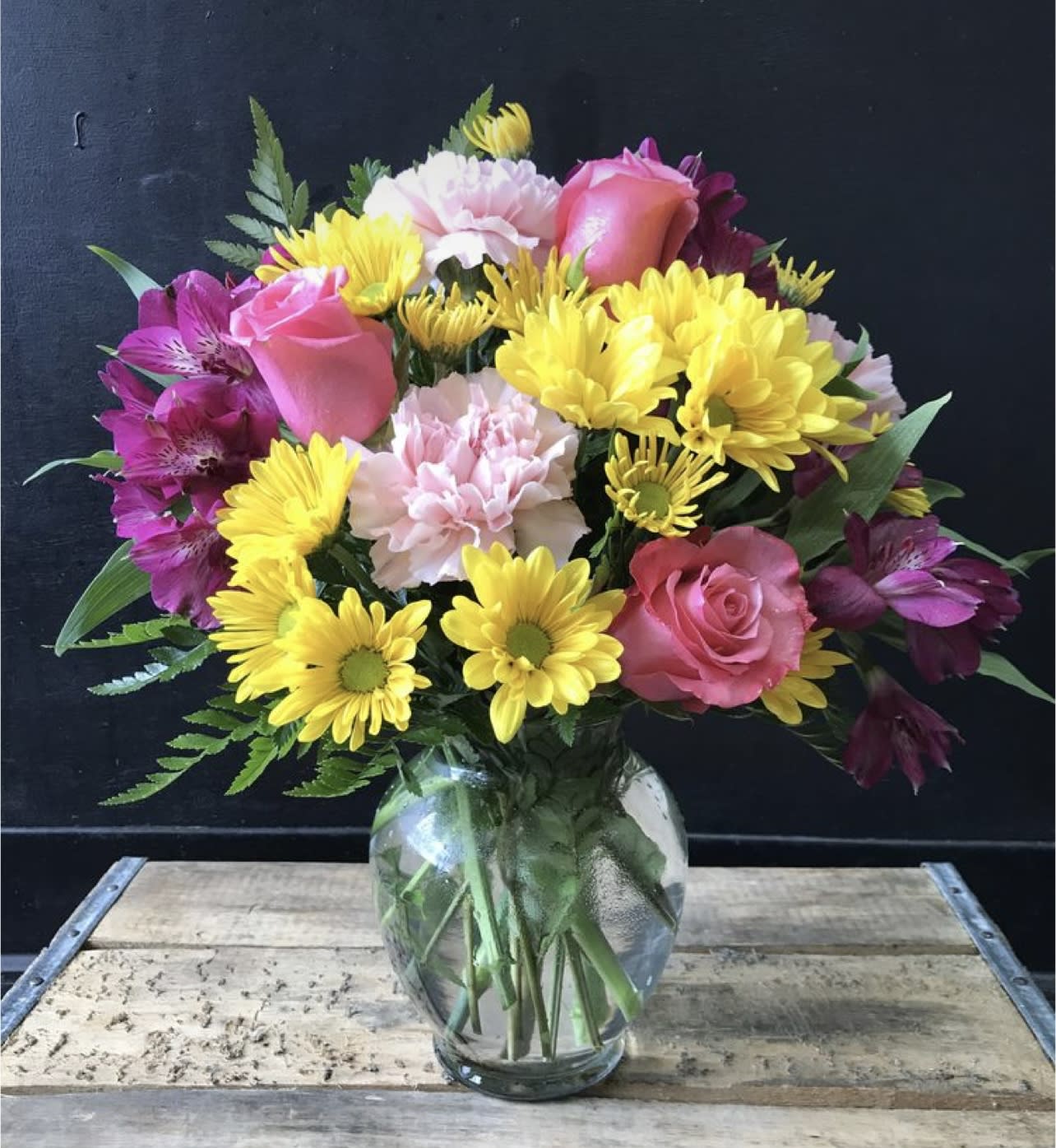 Mixed bouquet of pink roses, yellow daisies, and purple alstroemeria in a glass vase