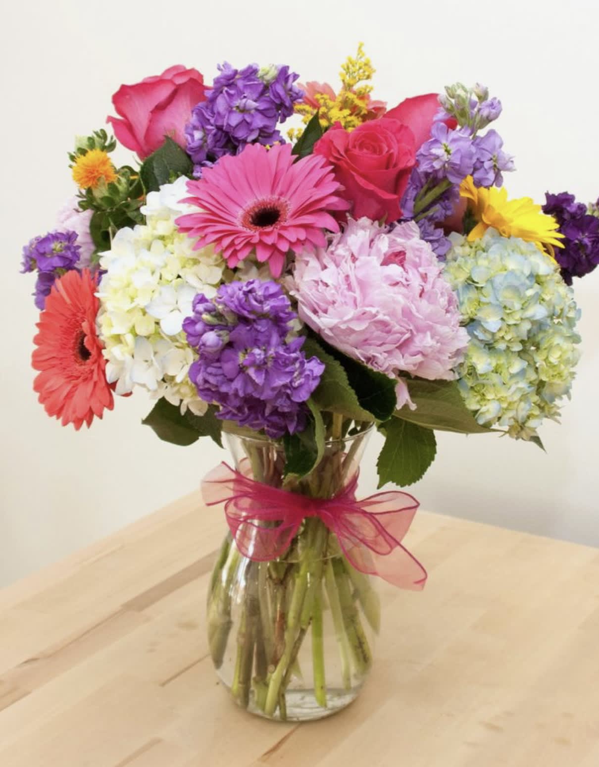 Colorful mixed bouquet in a glass vase with a pink ribbon