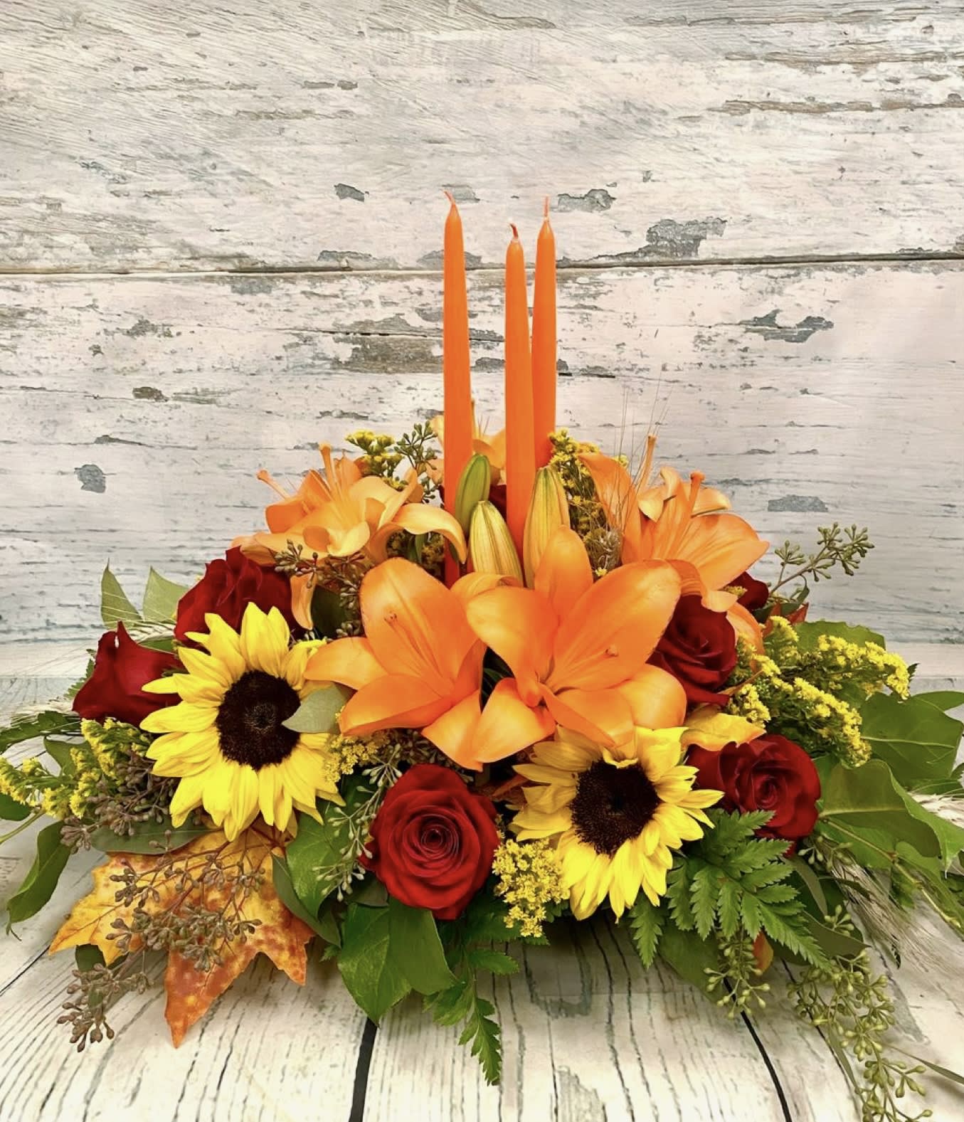 Orange lilies and red roses with sunflowers in a low arrangement.