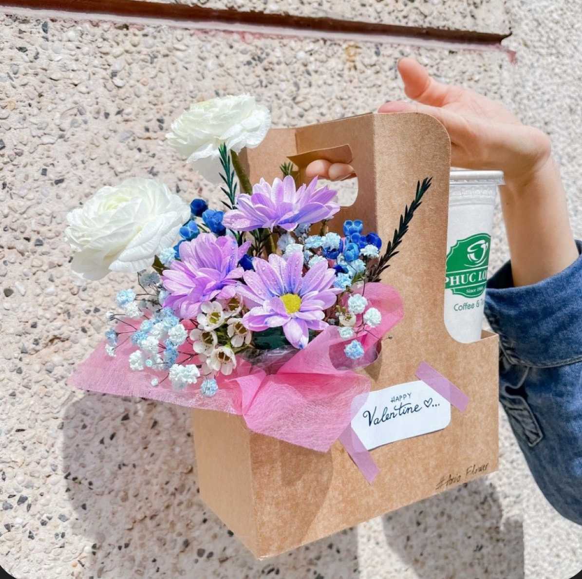 Bouquet of white and purple flowers in a kraft gift bag with a drink cup