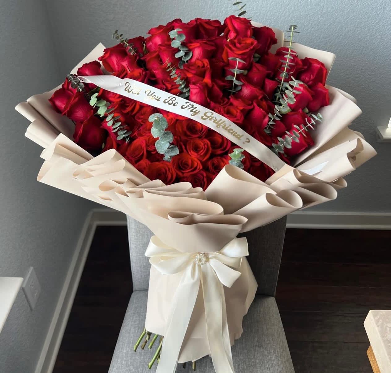 Large bouquet of red roses wrapped in cream paper with a ribbon