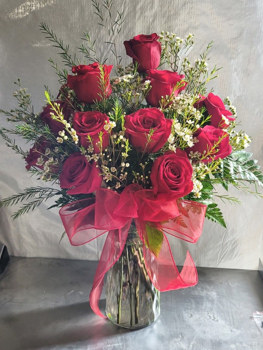 Red roses in a clear glass vase with a pink ribbon