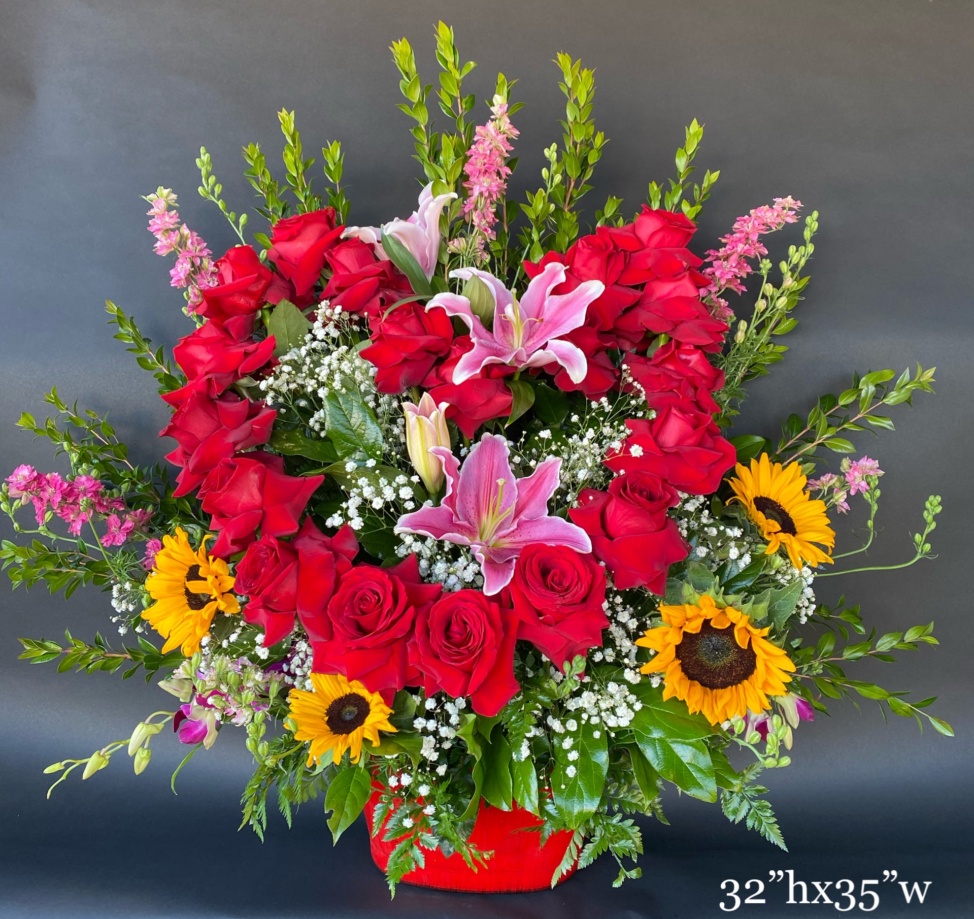 Large red rose and pink lily arrangement with sunflowers in a red container