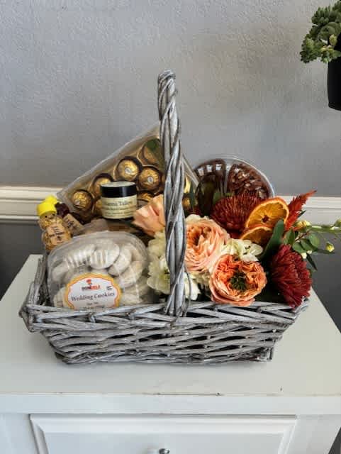Gift basket with flowers, cookies, chocolates, and a candle in a wicker basket