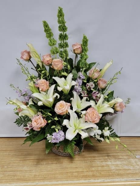 Large floral arrangement with white lilies, peach roses, and purple accents in a basket