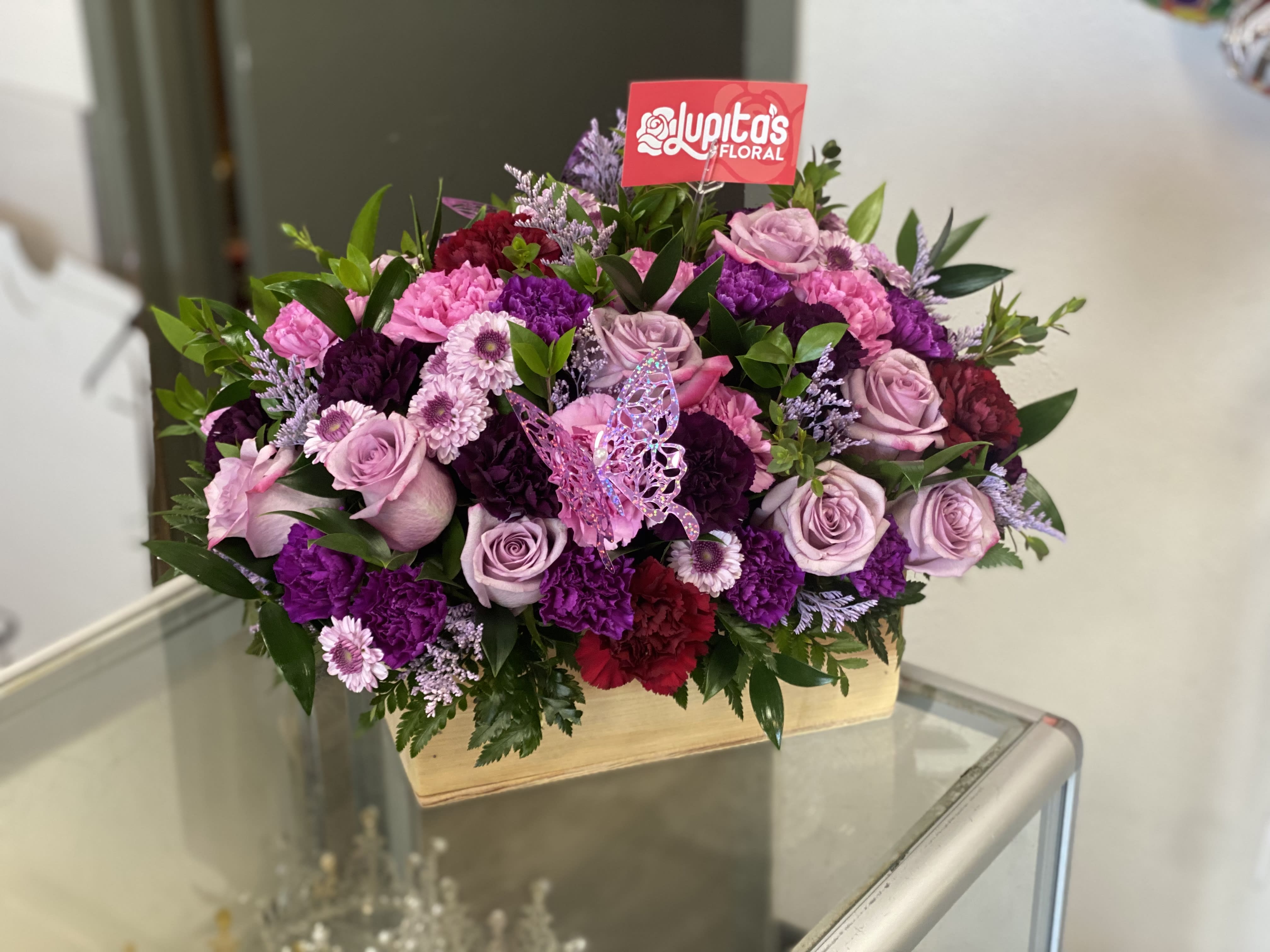 Pink and purple floral arrangement in a wooden box with a butterfly pick