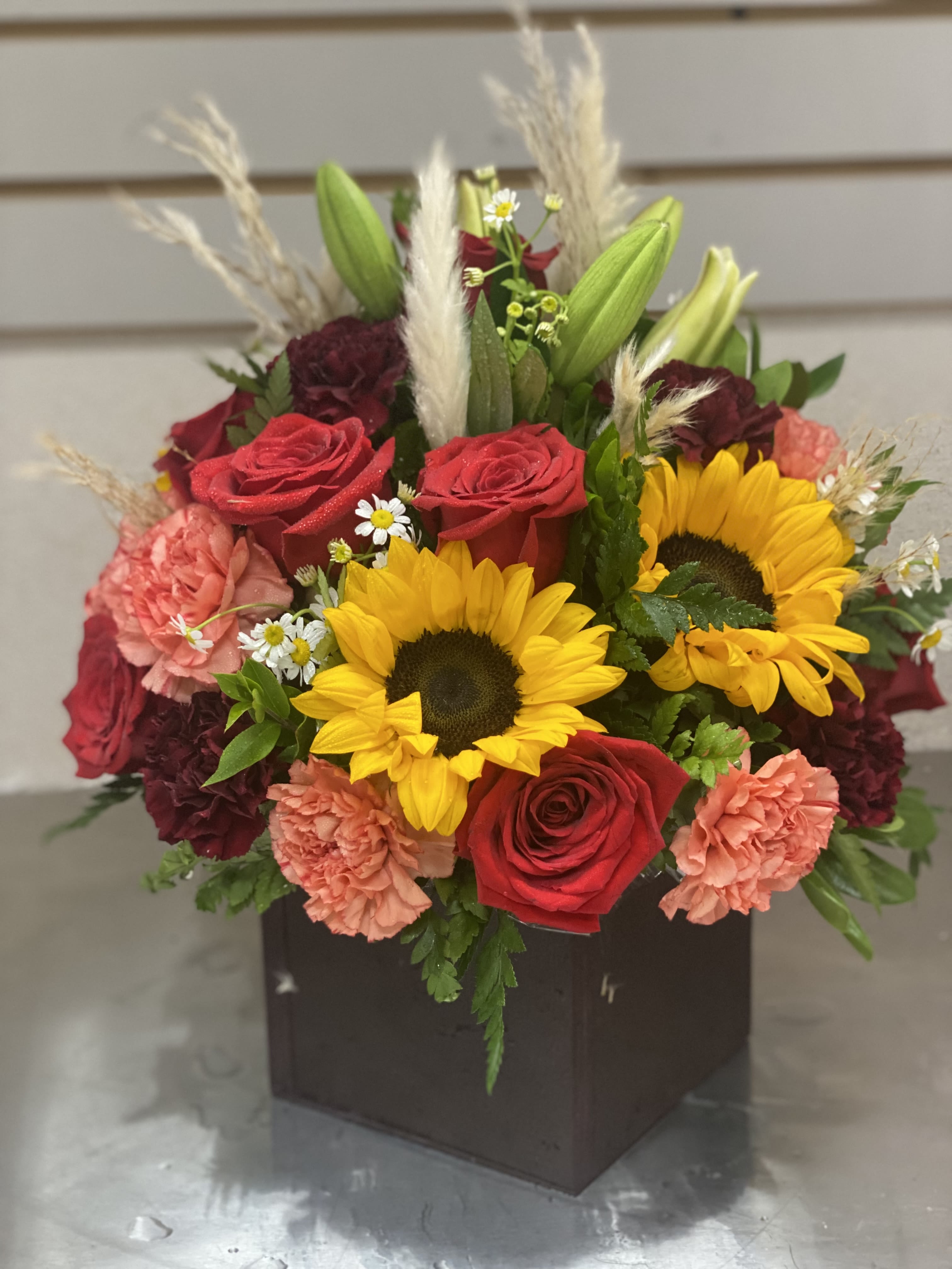 Bouquet of sunflowers, red roses, and pink carnations in a dark box vase