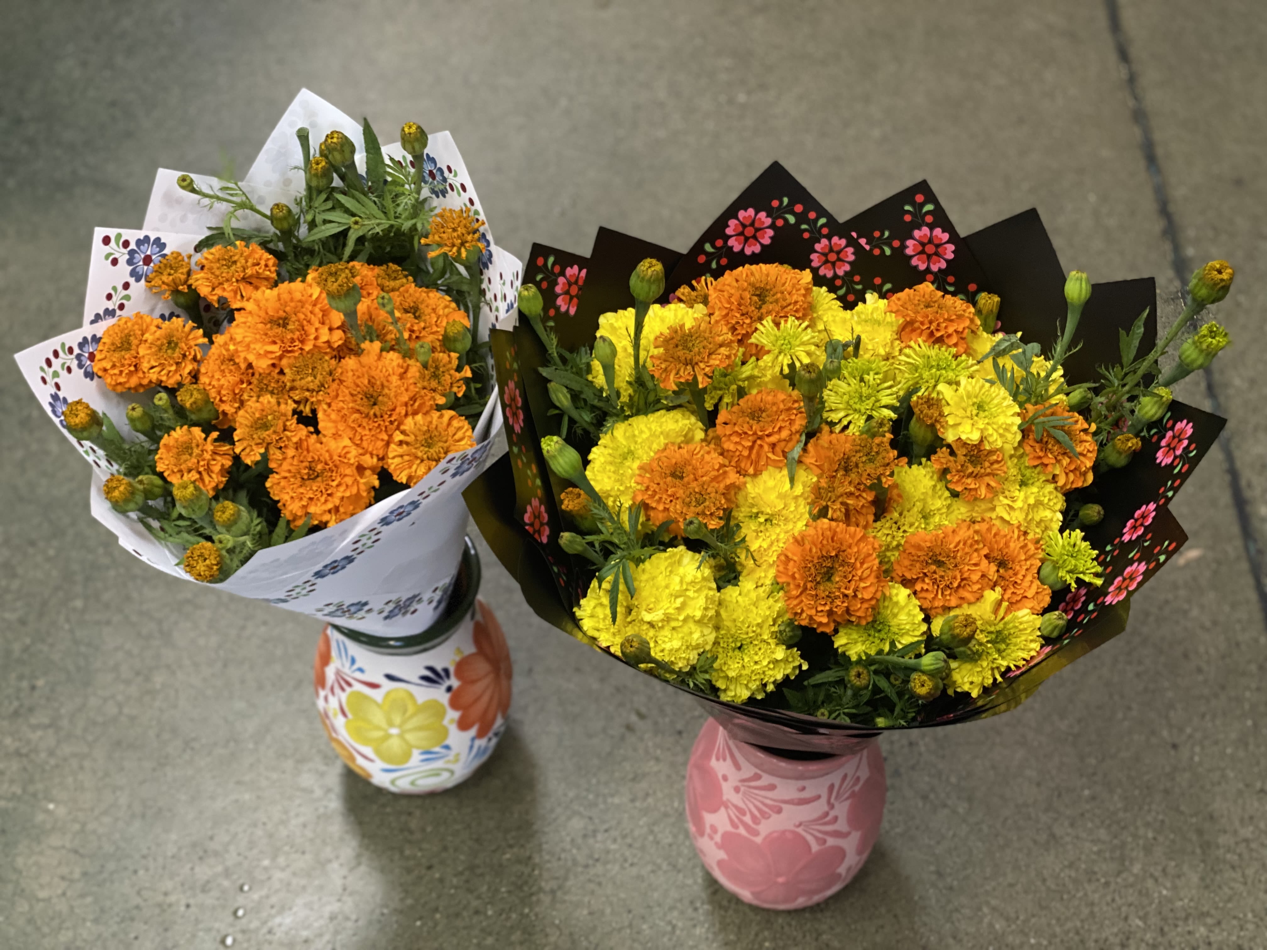 Two marigold bouquets in painted ceramic vases on a concrete floor