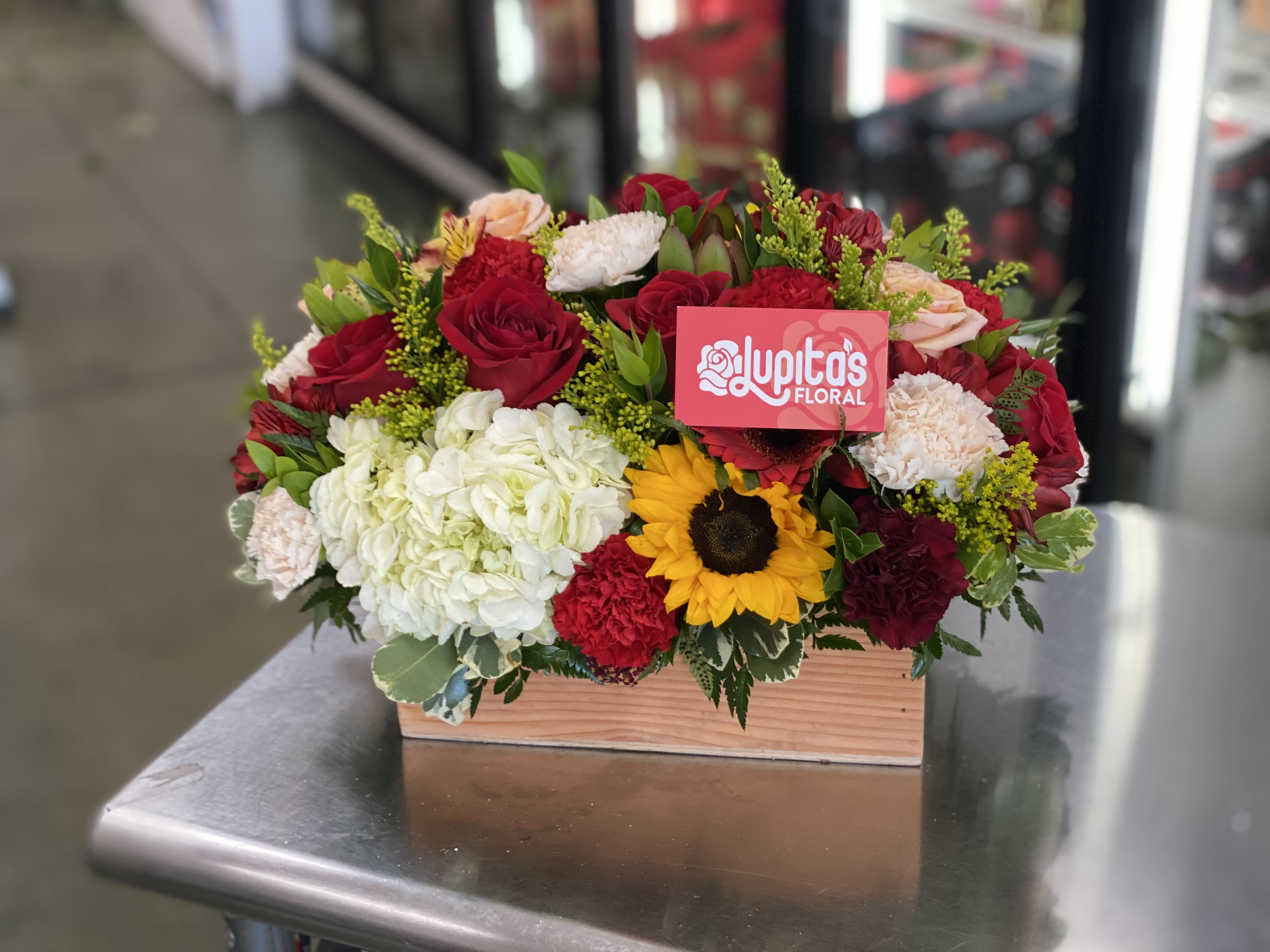 Mixed bouquet in a wooden box with red roses, white hydrangea, and a sunflower