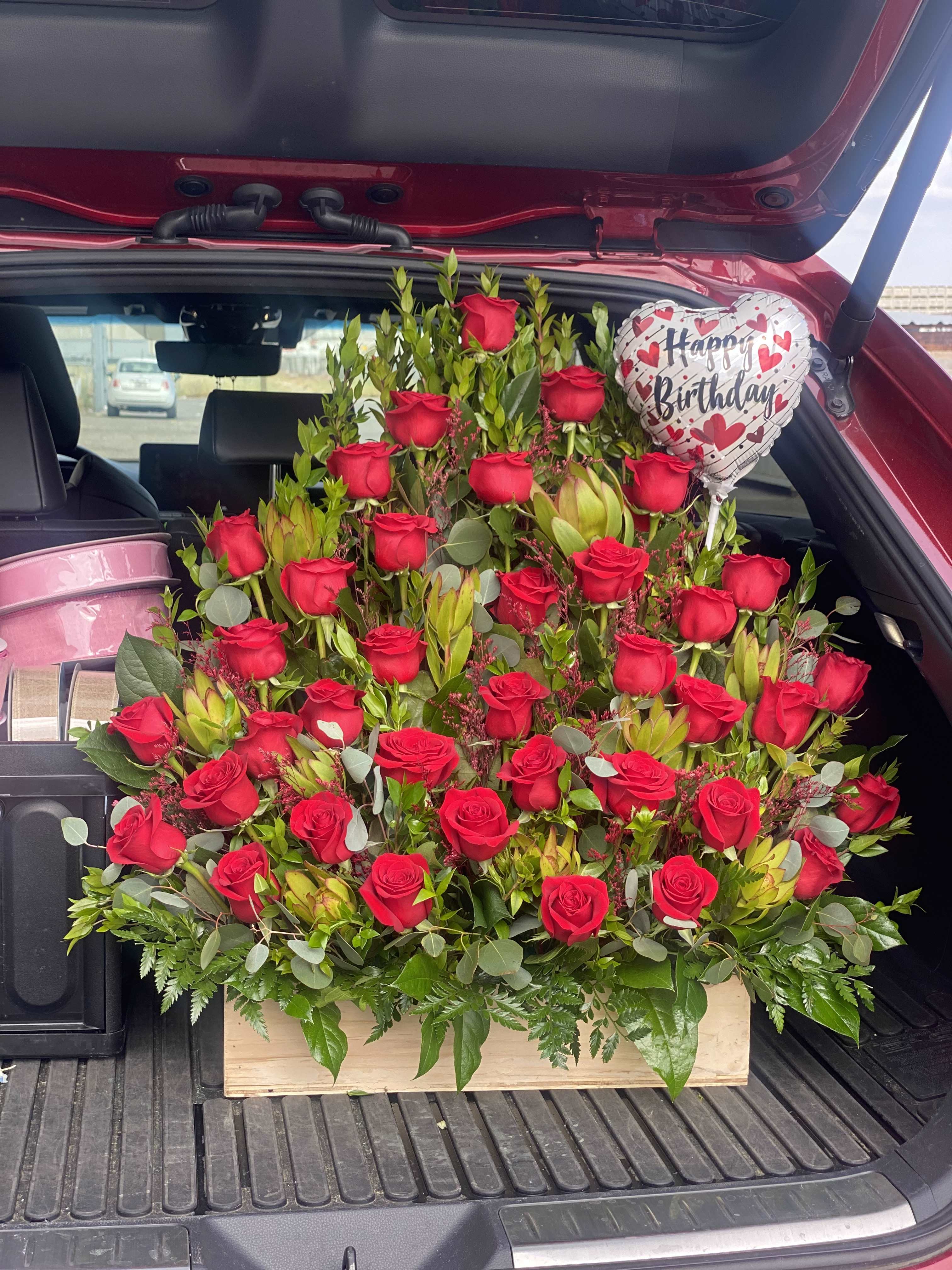 Large bouquet of red roses with a birthday balloon in a car trunk