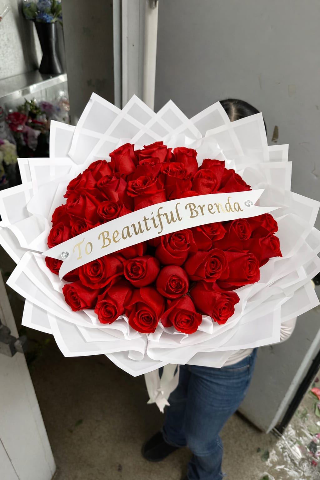 Large bouquet of red roses wrapped in white paper with a name ribbon