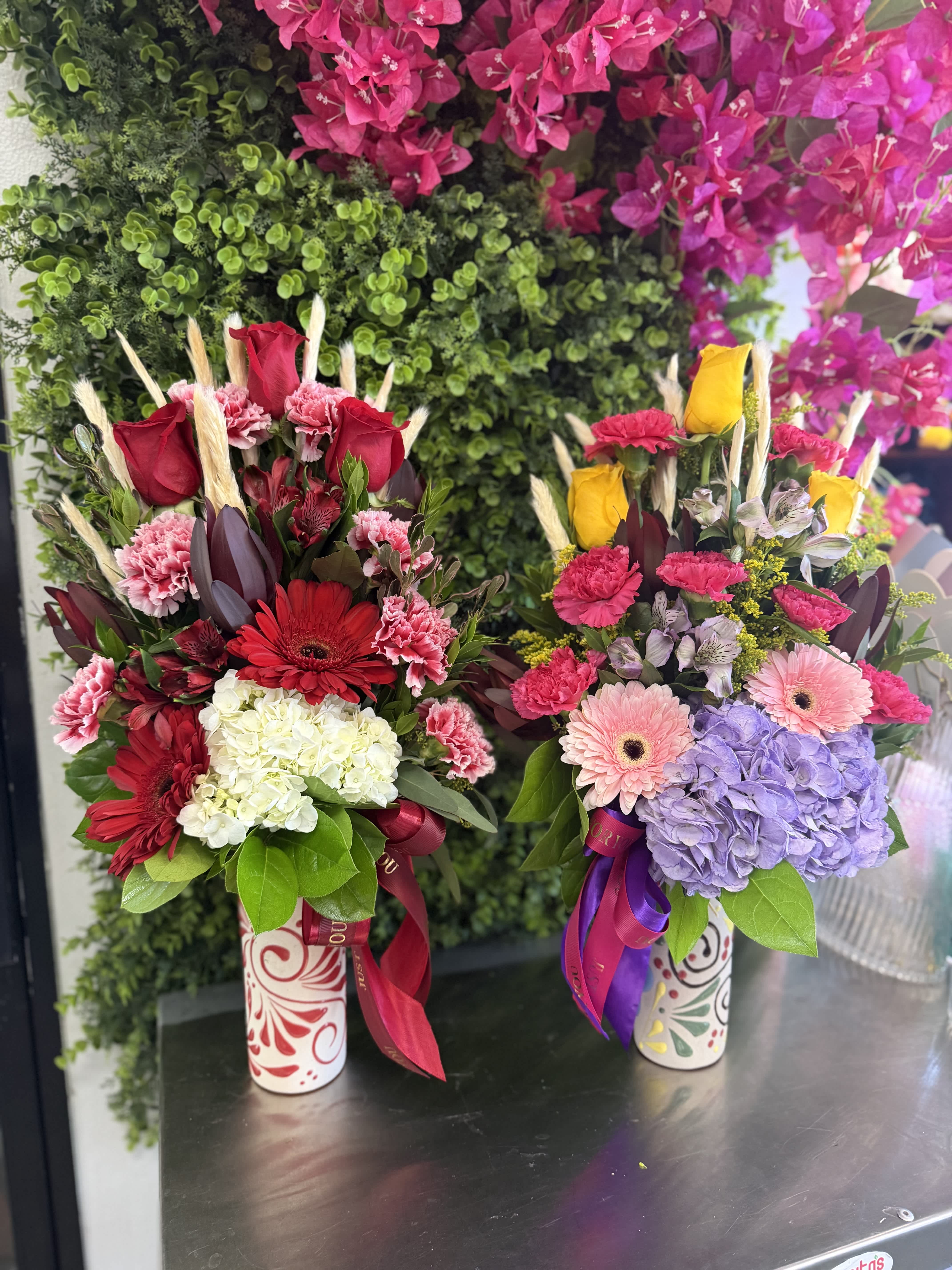 Two colorful floral arrangements in patterned vases with ribbons