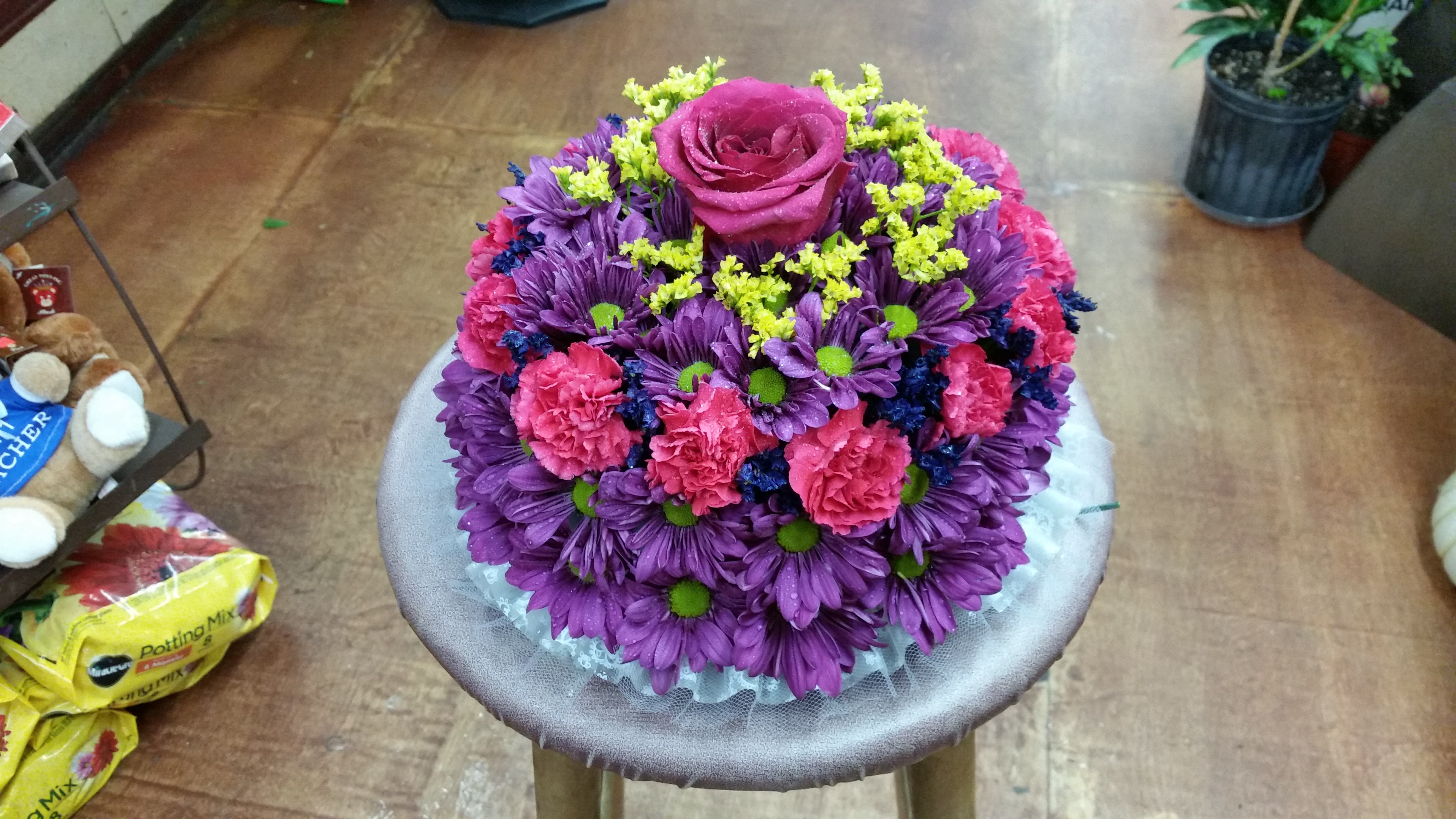 Round bouquet of purple and pink flowers with a magenta rose on top