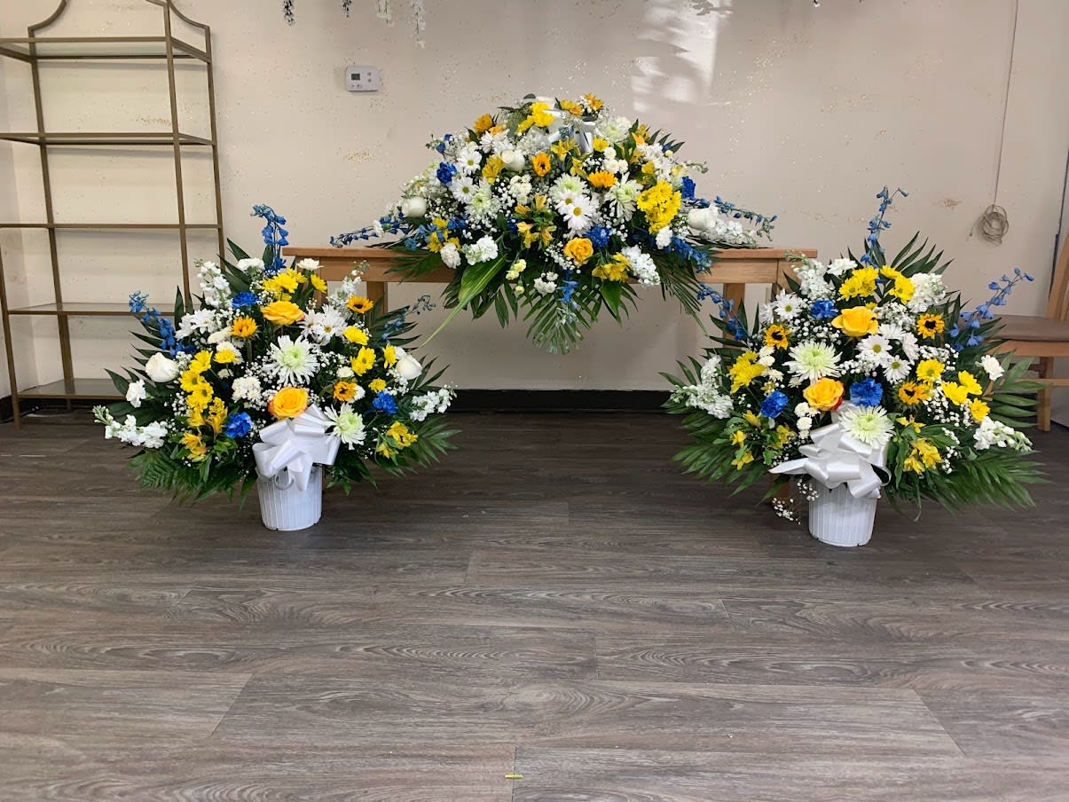 Three floral funeral arrangements with white, yellow, and blue flowers