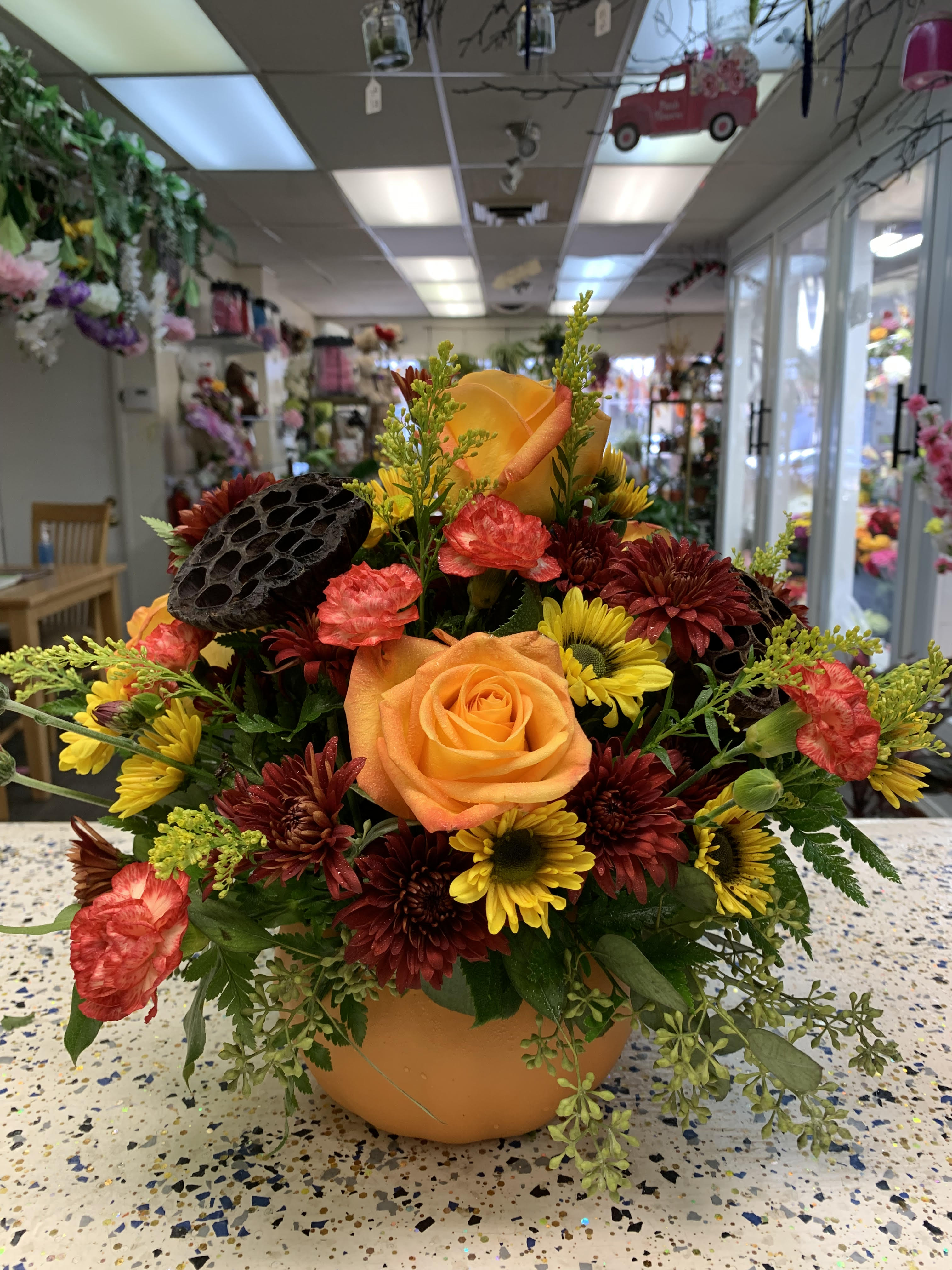 Orange rose arrangement with yellow and burgundy flowers in a pumpkin-shaped container
