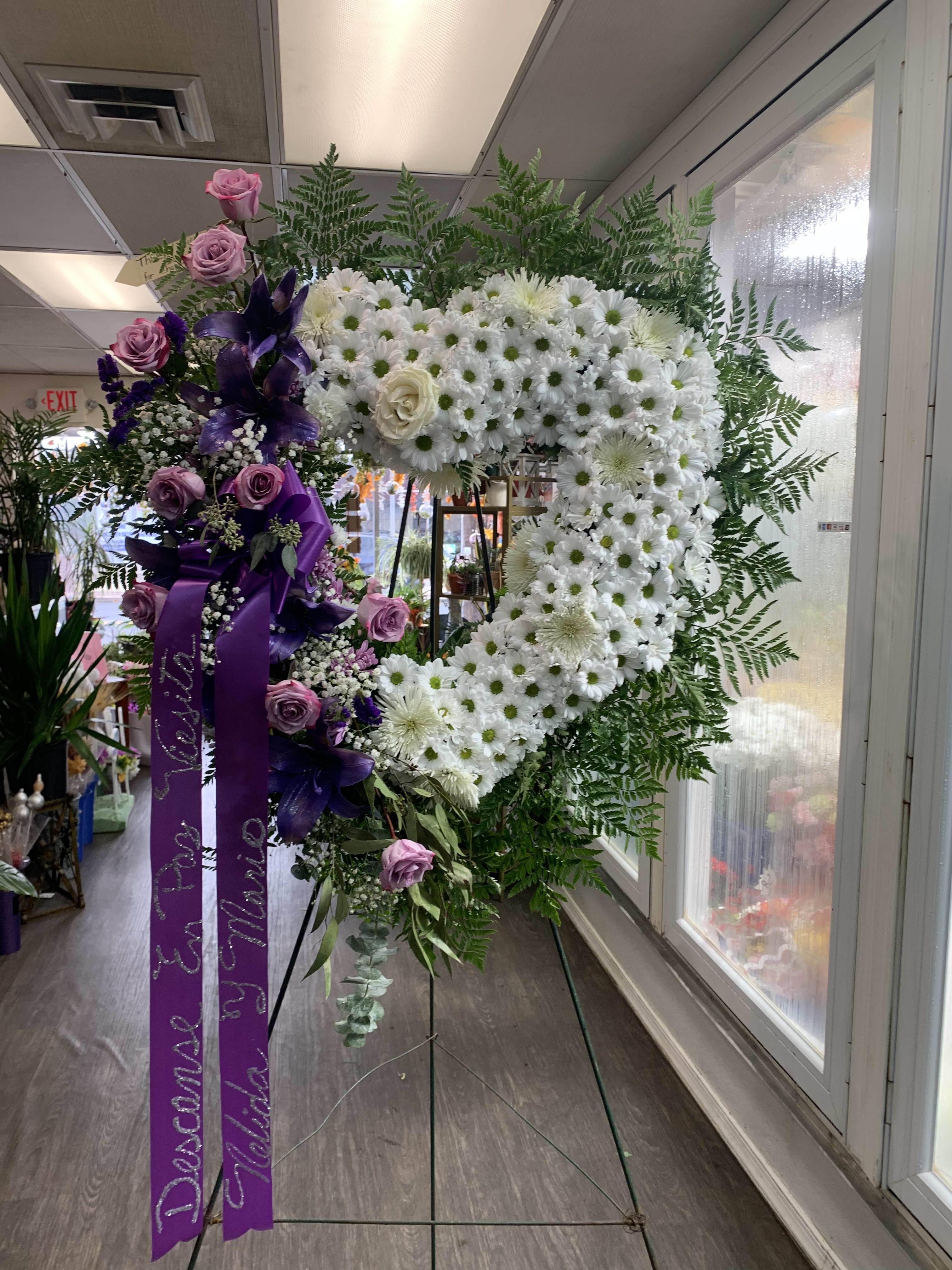 Heart-shaped floral wreath with white daisies and purple roses on an easel