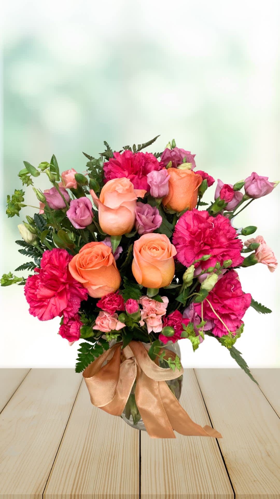 Bouquet of orange roses and pink carnations in a glass vase with ribbon