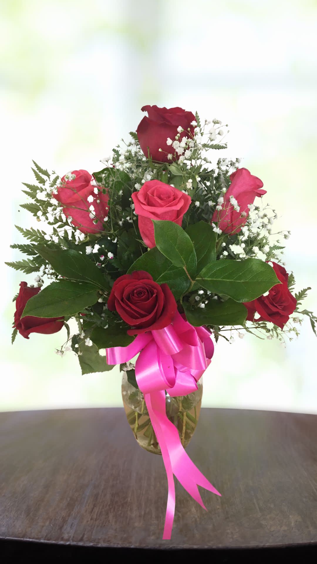 Red roses in a glass vase with a pink ribbon