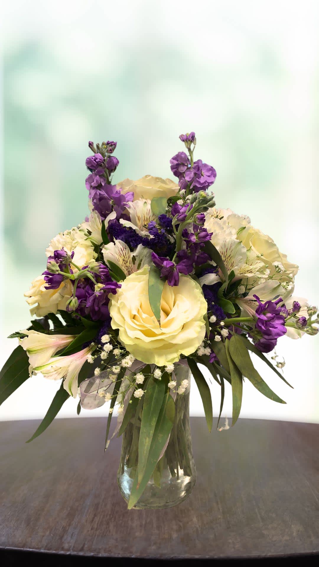 Bouquet of pale yellow roses and purple flowers in a glass vase