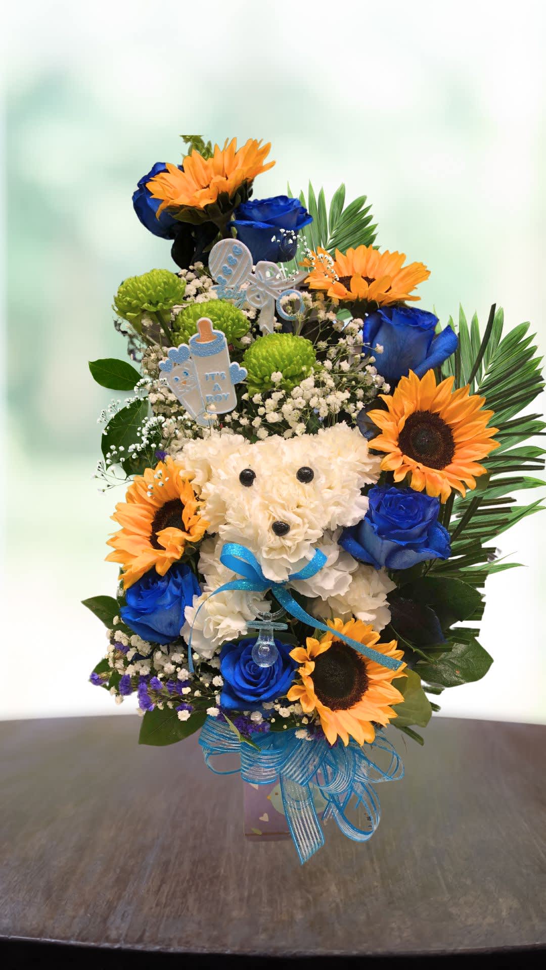 Blue roses and sunflowers arranged around a white teddy bear