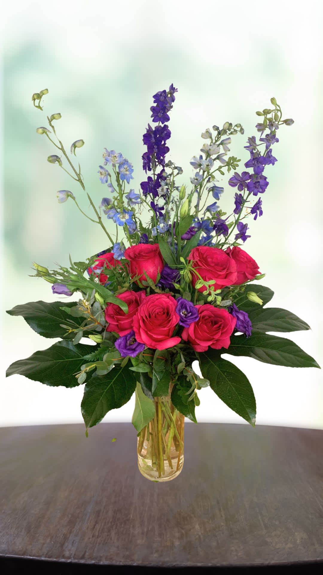 Pink roses and purple flowers arranged in a clear glass vase