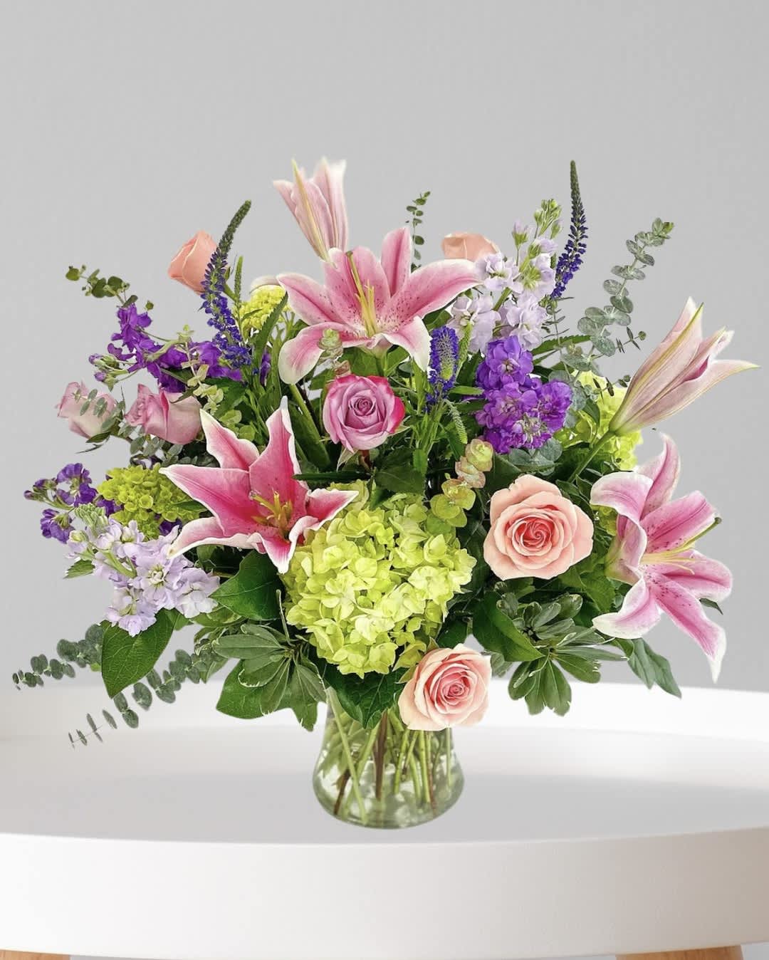 Mixed bouquet of pink lilies, roses, and purple flowers in a glass vase