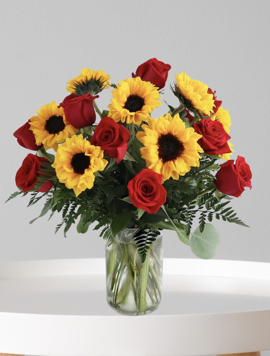 Red roses and yellow sunflowers in a clear glass vase