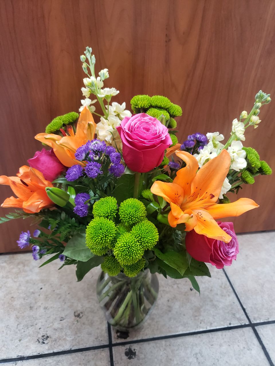 Bouquet of pink roses, orange lilies, and green chrysanthemums in a glass vase