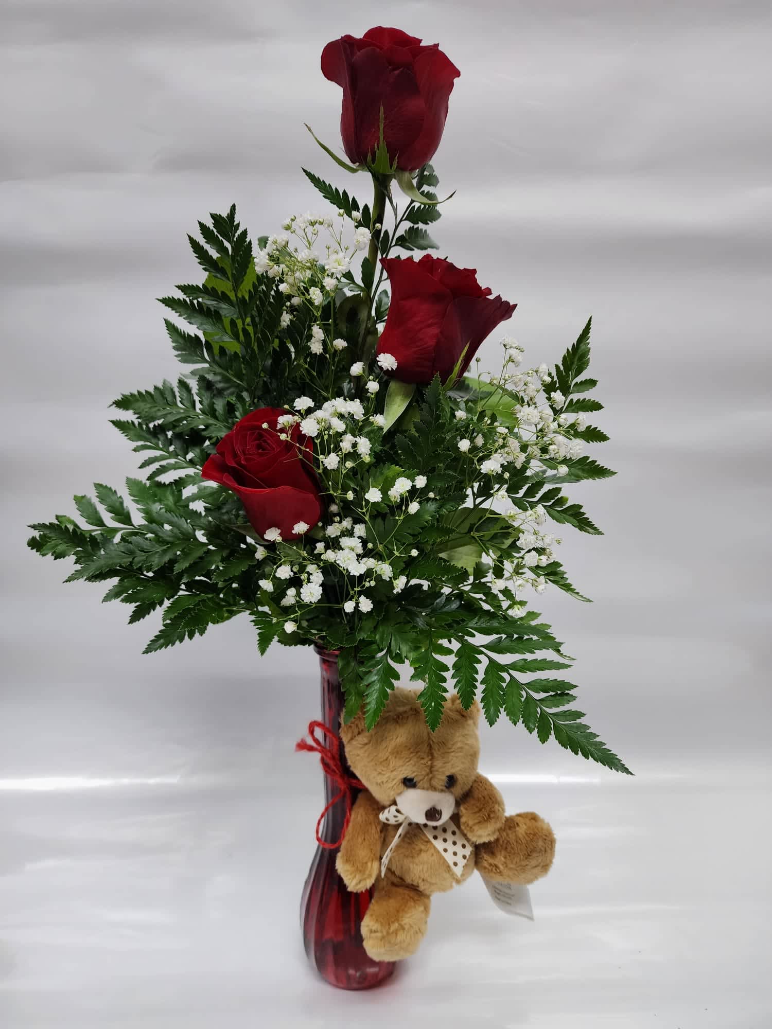 Red roses in a tall vase with baby's breath and a teddy bear