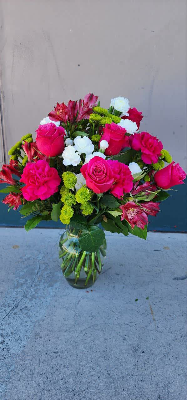 Bouquet of pink roses, white blooms, and green button mums in a glass vase