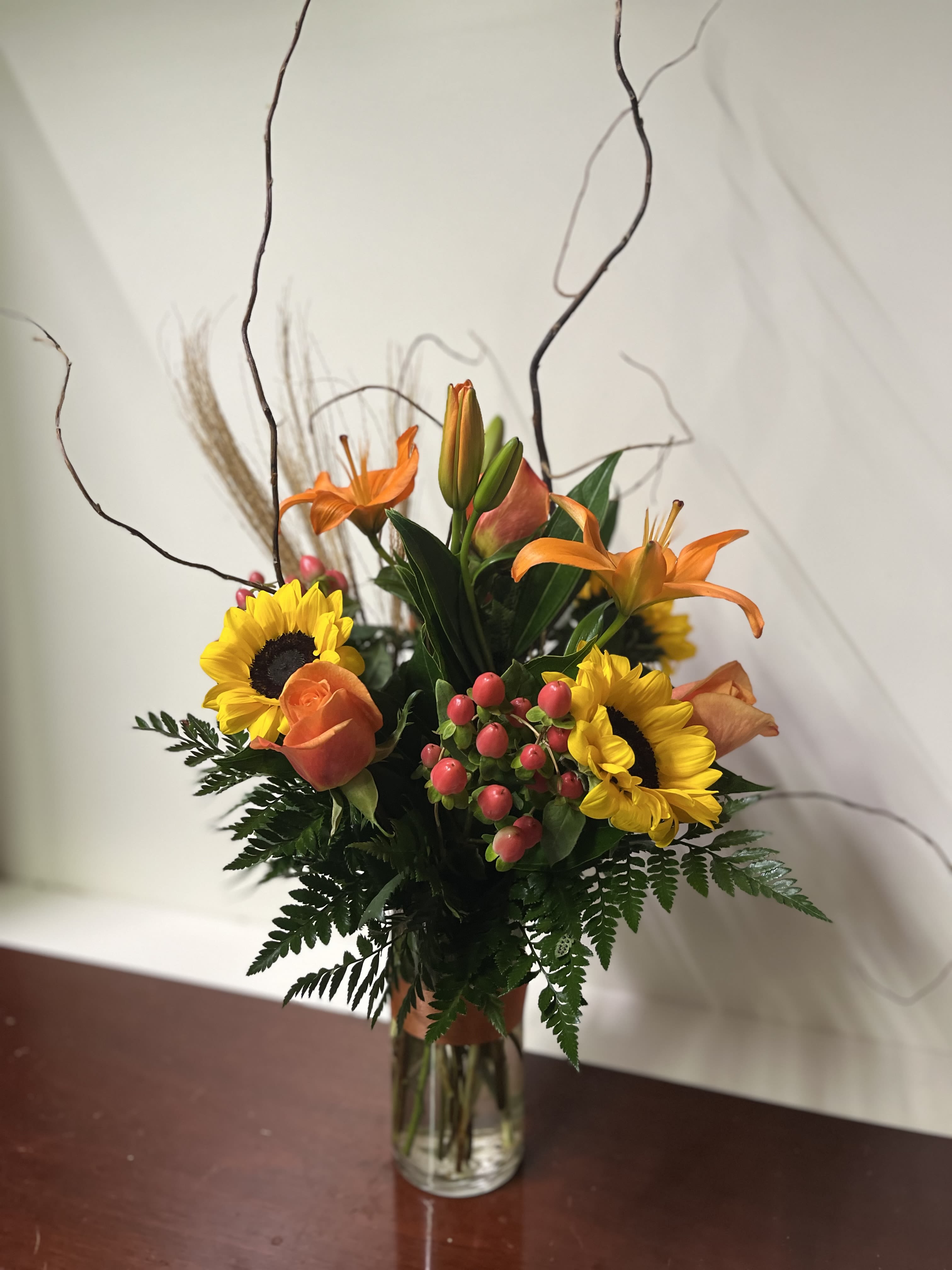 Orange lilies and sunflowers arranged in a clear glass vase