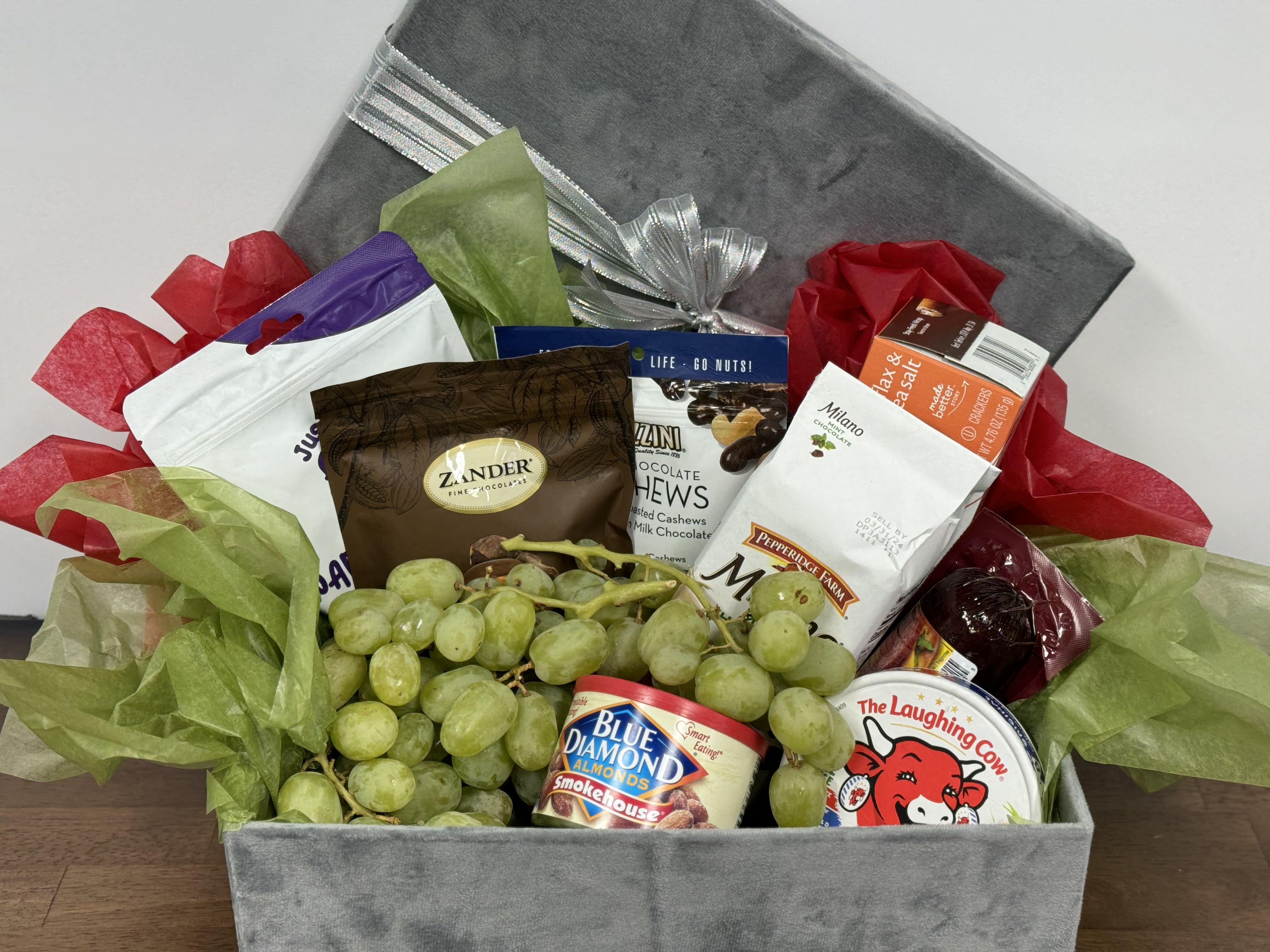Gift basket with grapes, snacks, and a gray lid tied with silver ribbon