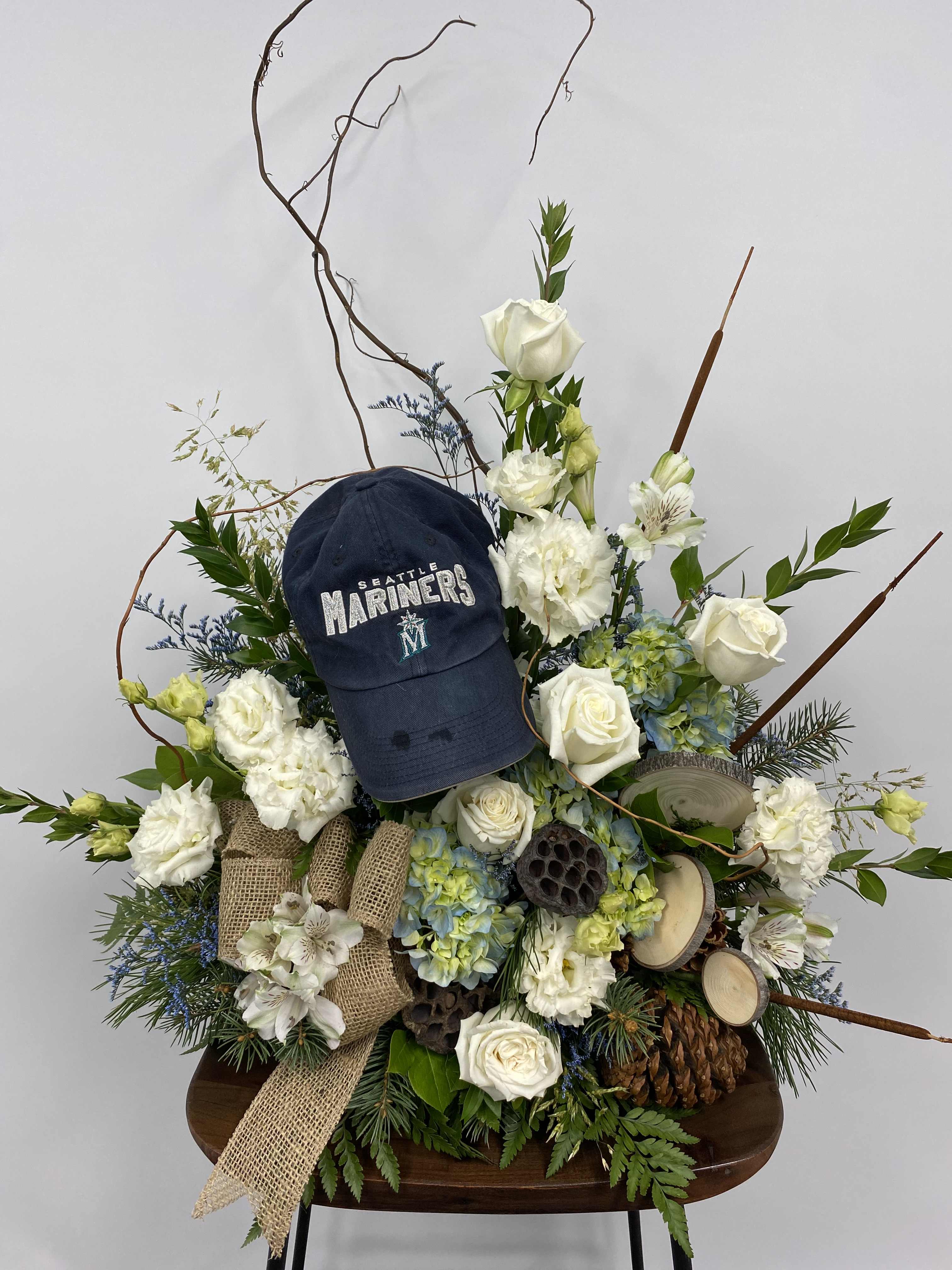 Floral arrangement with white roses, hydrangeas, and a Seattle Mariners cap